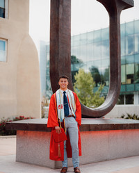 Image of Andrew Norton in his graduation regalia standing in front of the U statue located on central campus in front of Hodgin Hall.