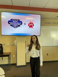 Image of Daniela Palomino in Jackson Student Center in front of a tv screen that says Fastenal National Sales invitational logo with the Professional Sales Association logo.